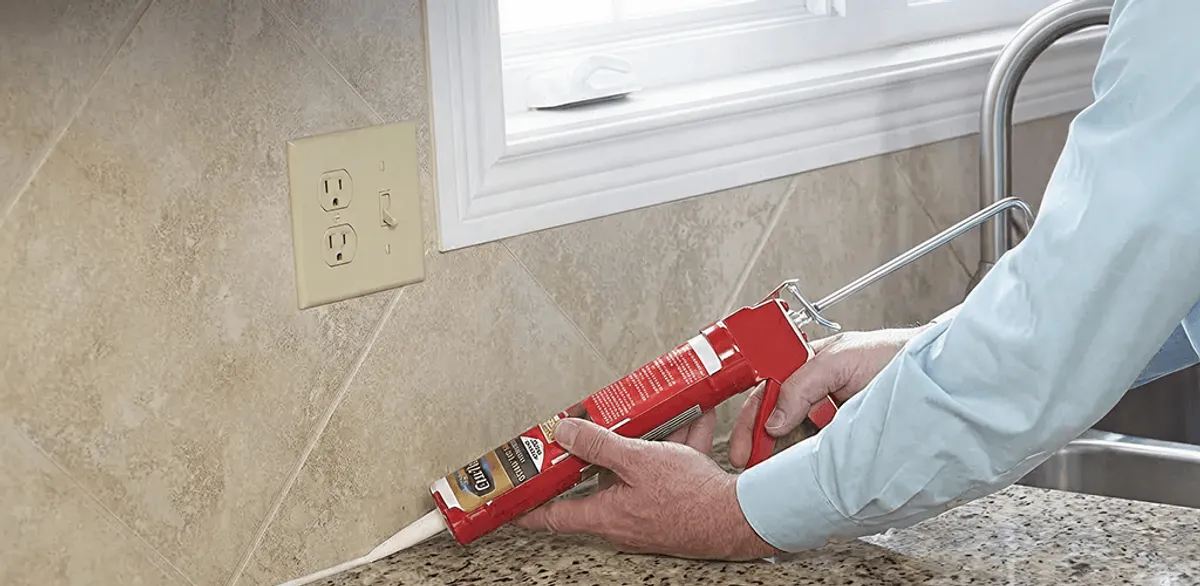 Handyman applying caulk along a kitchen backsplash and countertop seam in Chicago, IL